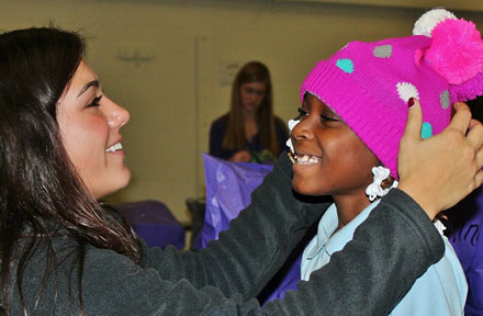Prairie Ridge Student Council member Riley Corcoran tries a hat on a Lyon Magnet Elementary student during the Caring for Kids Winter Clothing Drive on November 25, 2013.