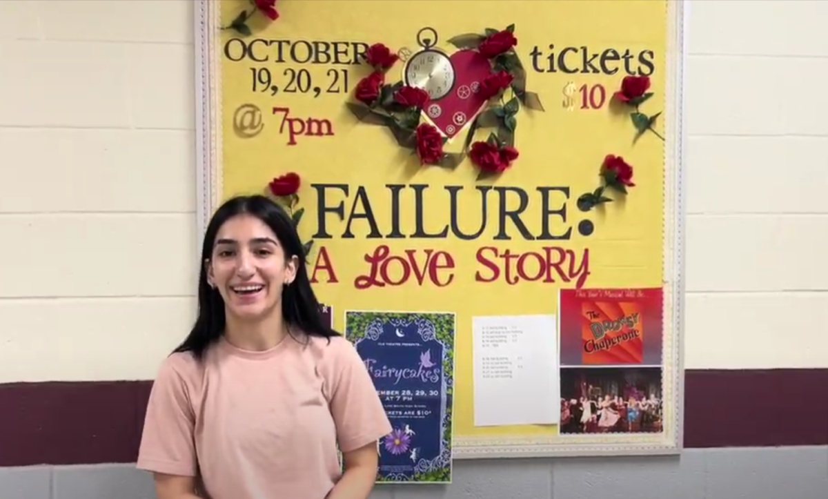 Ellen Iremashvili stands in front of the 2023 Prairie Ridge High School fall play bulletin board to introduce her video interview of the cast and crew.